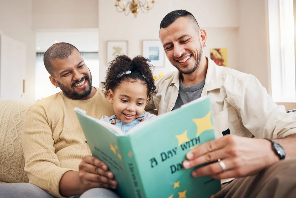 two male foster parents reading story book to young girl
